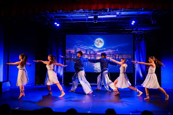 Ensemble in white and blue costumes in a diagonal line under a moonlit backdrop