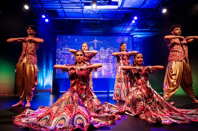 Performers seated in a fan formation in richly patterned lehengas